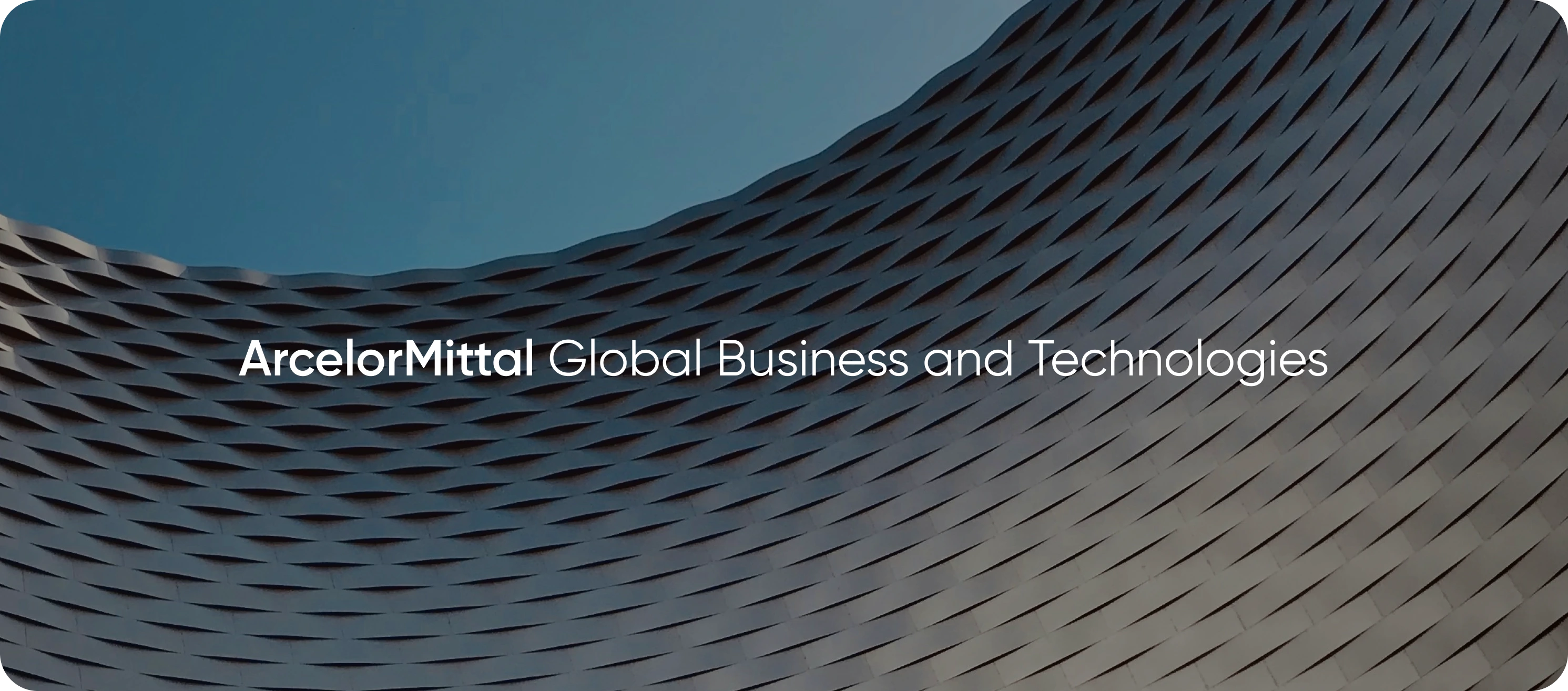 The AMGBT lockup — ArcelorMittal Global Business and Technologies — set in white across the woven metal façade of an ArcelorMittal building.